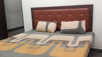 Una cama con cabecera capitonada, dos almohadas y una colcha estampada.