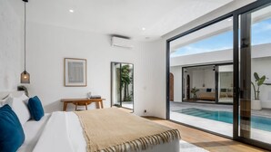 Un dormitorio con cama, escritorio y vista a una piscina a través de puertas de vidrio.