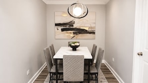 A dining area with a rectangular table, six chairs, a chandelier, and a wall-mounted abstract painting. - Spacious 5BD 2BA Home Close To Oakbrook (Westmont)