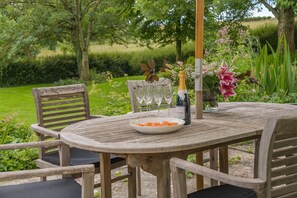 An outdoor wooden table with chairs, a bottle of champagne, and a plate of food. - 4 Bed in Chebbard (oc-c43270) (Puddletown)