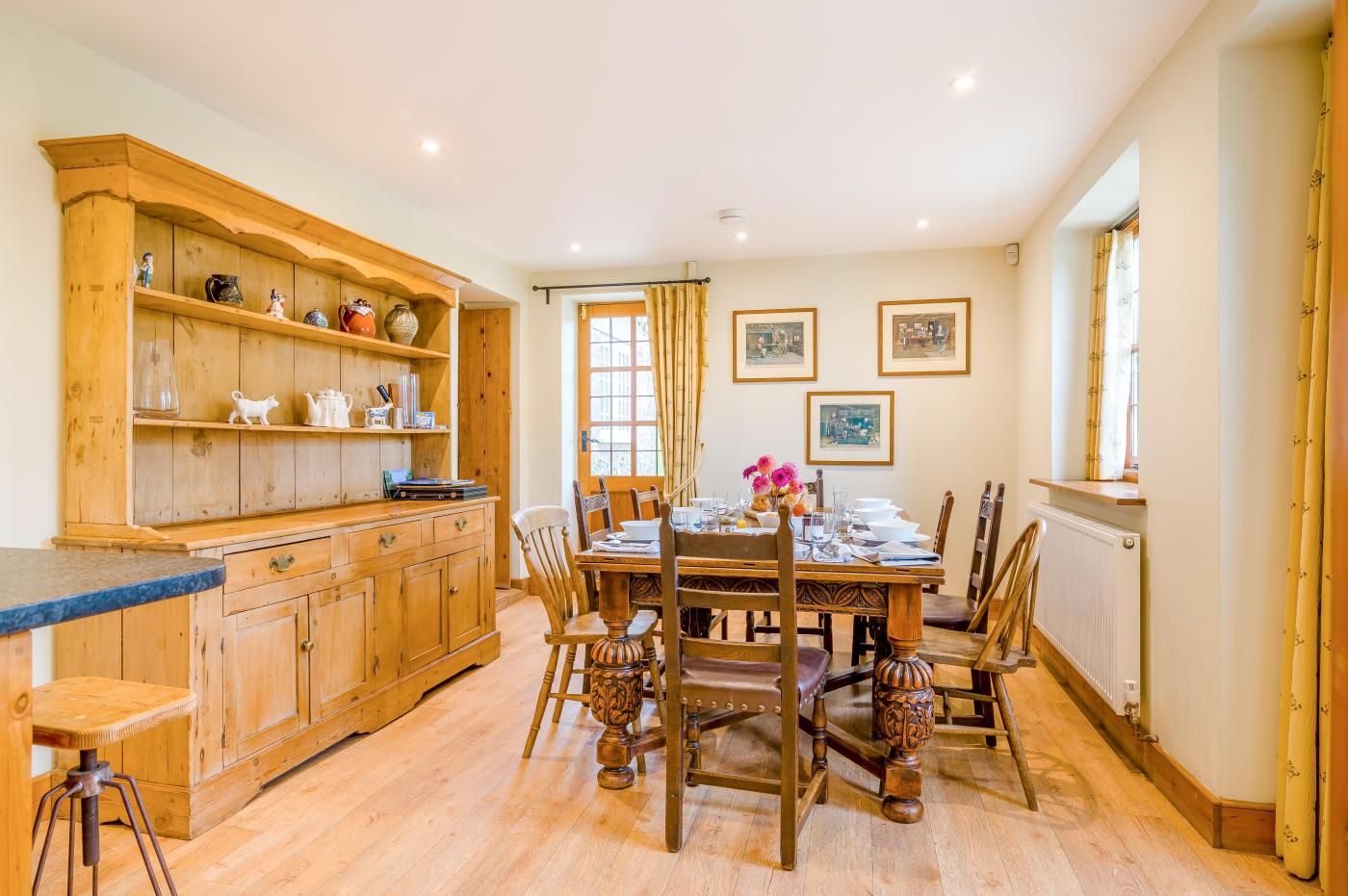 Een traditionele keuken met houten keukenkastjes, een eettafel gedekt voor vier personen en een raam met gordijnen.