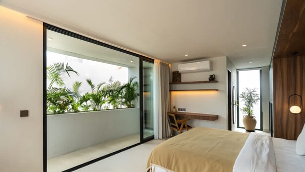 Un dormitorio moderno con una cama grande, un escritorio y vistas a la vegetación a través de un ventanal corredera.