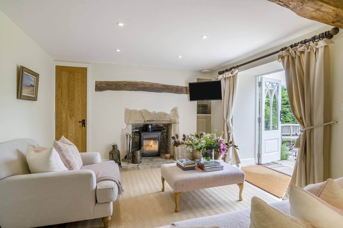 A cozy living room with a fireplace, a sofa, a coffee table with books and flowers, and a television.