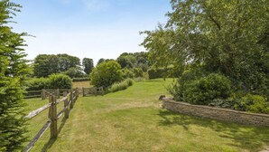 A grassy outdoor area with a wooden fence and stone wall, surrounded by trees and shrubs. - 1 Bed in Chebbard (oc-p43271) (Puddletown)
