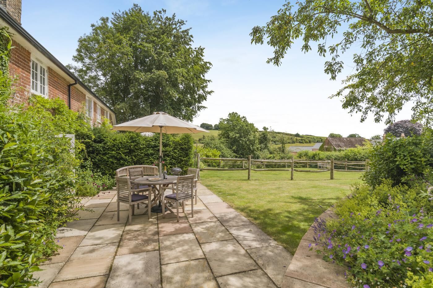 A patio with a table and chairs, surrounded by greenery and a fence.