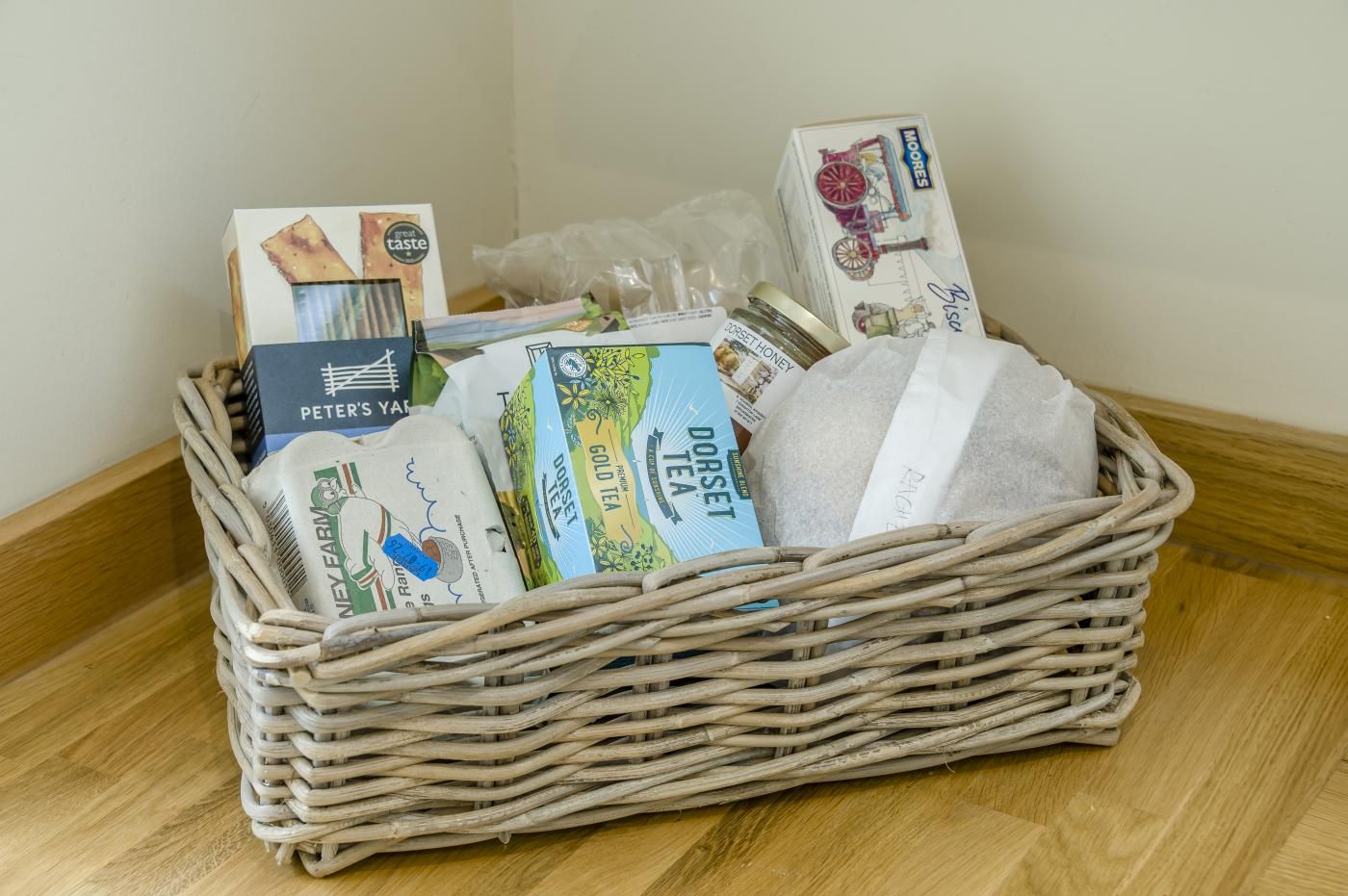 Een rieten mand gevuld met verschillende verpakte etenswaren en een pot honing op een houten vloer.