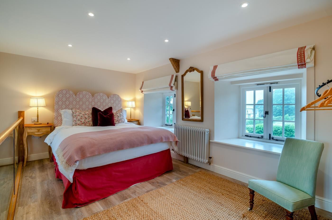 Une chambre à coucher avec un lit, des tables de chevet, un radiateur, une fenêtre donnant sur un beau paysage et une chaise.