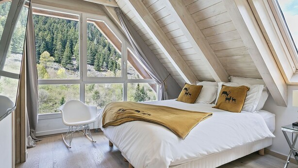 A bedroom with a large window, a bed with white bedding and two decorative pillows, a white chair, and a glass table. - Luderna - Dúplex Val de Ruda C37 Malh Blanc (Baqueira)