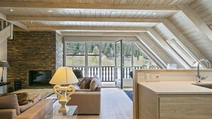 A spacious loft with a stone fireplace, a sofa, a dining area, and a large window overlooking a forest. - Luderna - Dúplex Val de Ruda C37 Malh Blanc (Baqueira)