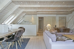 A loft-style living space with a high ceiling, a dining area with a chair and table, a sofa with cushions, and a lamp. - Luderna - Dúplex Val de Ruda C37 Malh Blanc (Baqueira)