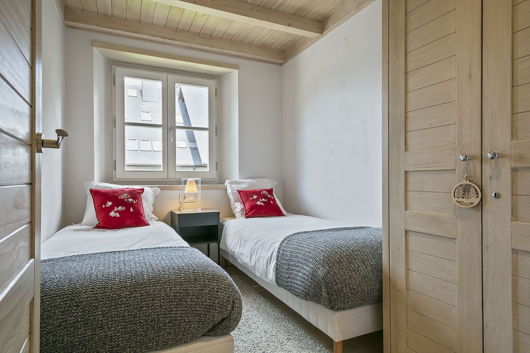A bedroom with two beds, a window, a nightstand, and a wooden door.