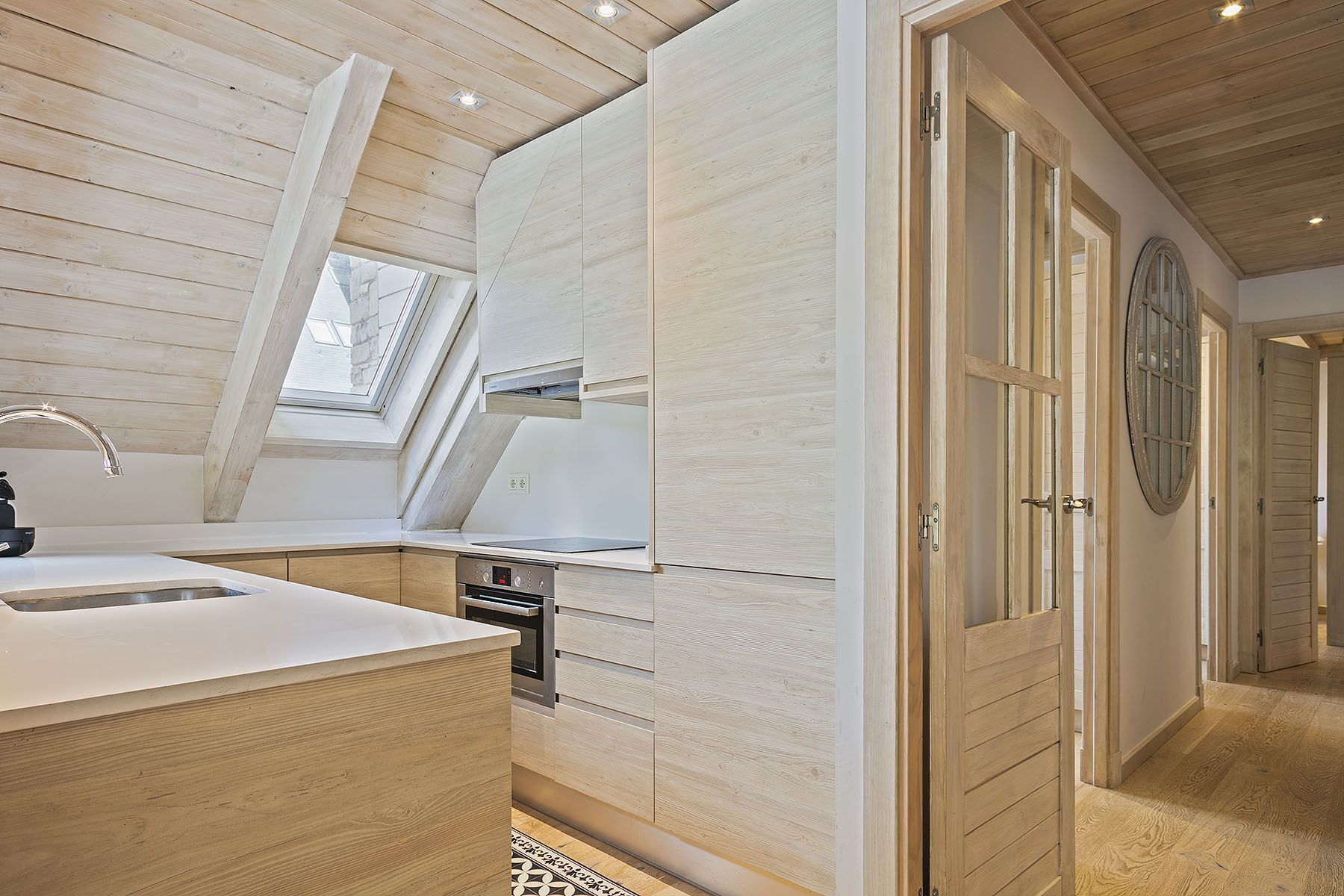 Een moderne keuken met houten kasten, een inbouwoven en een dakraam.