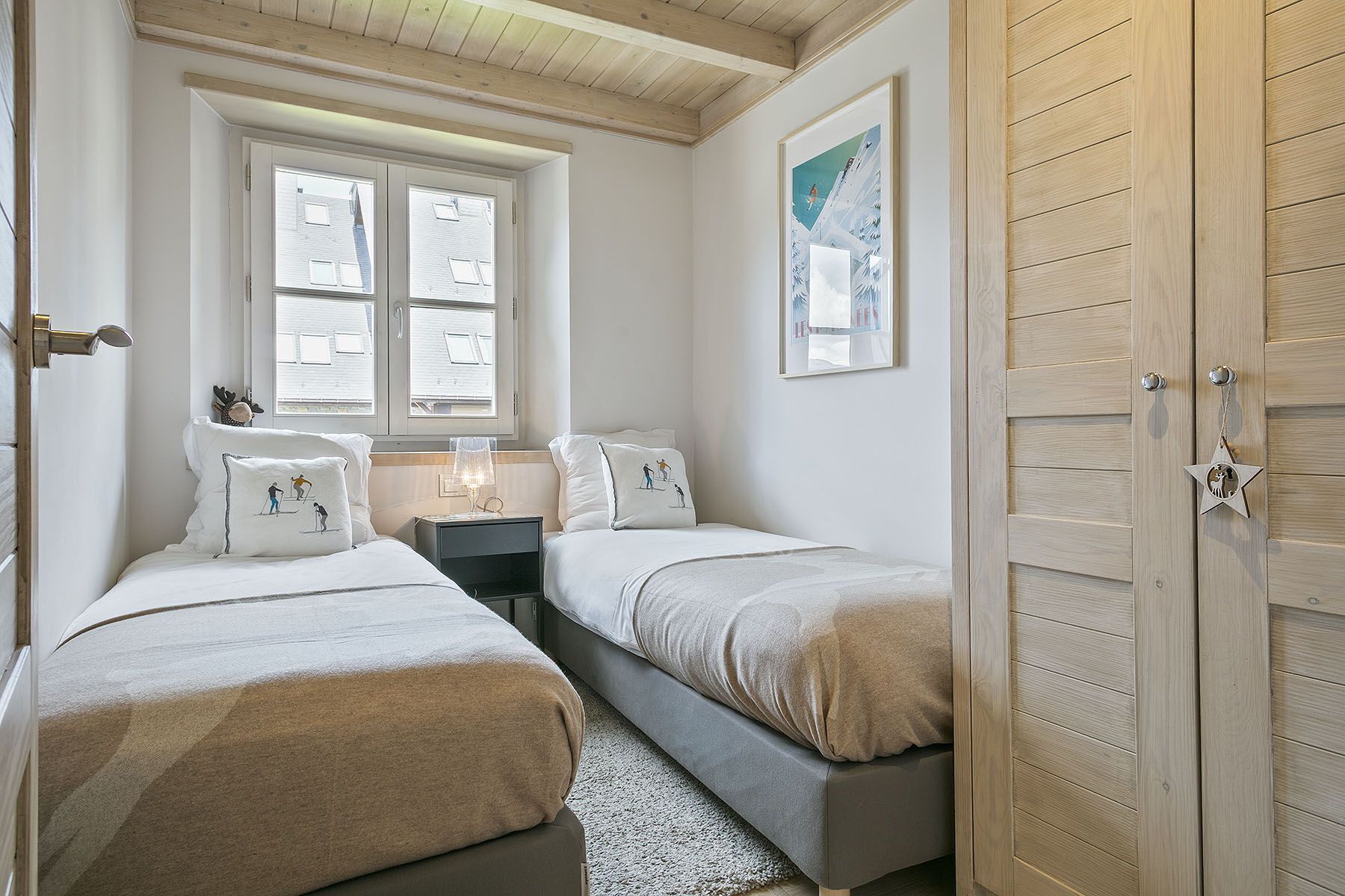 A bedroom with two beds, a window, a nightstand, a lamp, and a door.
