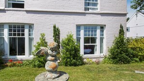 Un bâtiment à l’extérieur blanc, doté de grandes fenêtres et agrémenté d’un jardin où se trouve une sculpture.