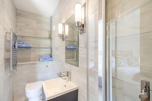 Ein modernes Badezimmer mit einer Duschkabine aus Glas, einem weißen Waschbecken und einem Spiegel mit Wandleuchten.