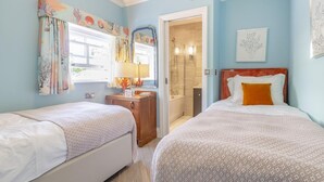 Une chambre avec deux lits, une commode en bois, un miroir et une salle de bain visible à travers une porte ouverte.