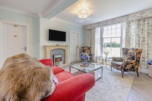 A living room with a fireplace, a television, and a large fur throw on a red sofa. - 2 Bed in Beaumaris (oc-l44702) (Beaumaris)