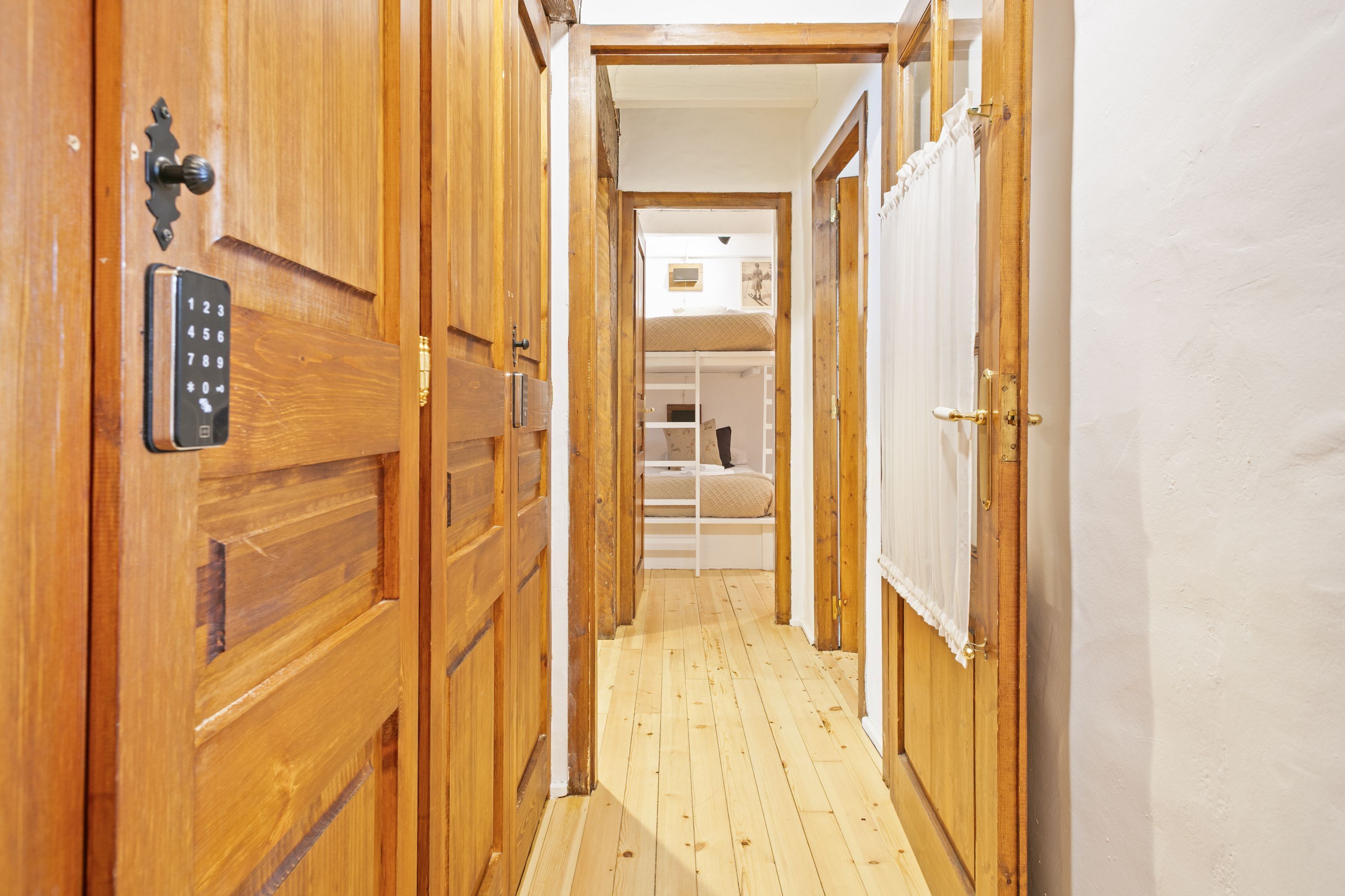 A wooden hallway leading to a bedroom with a bed and a window.