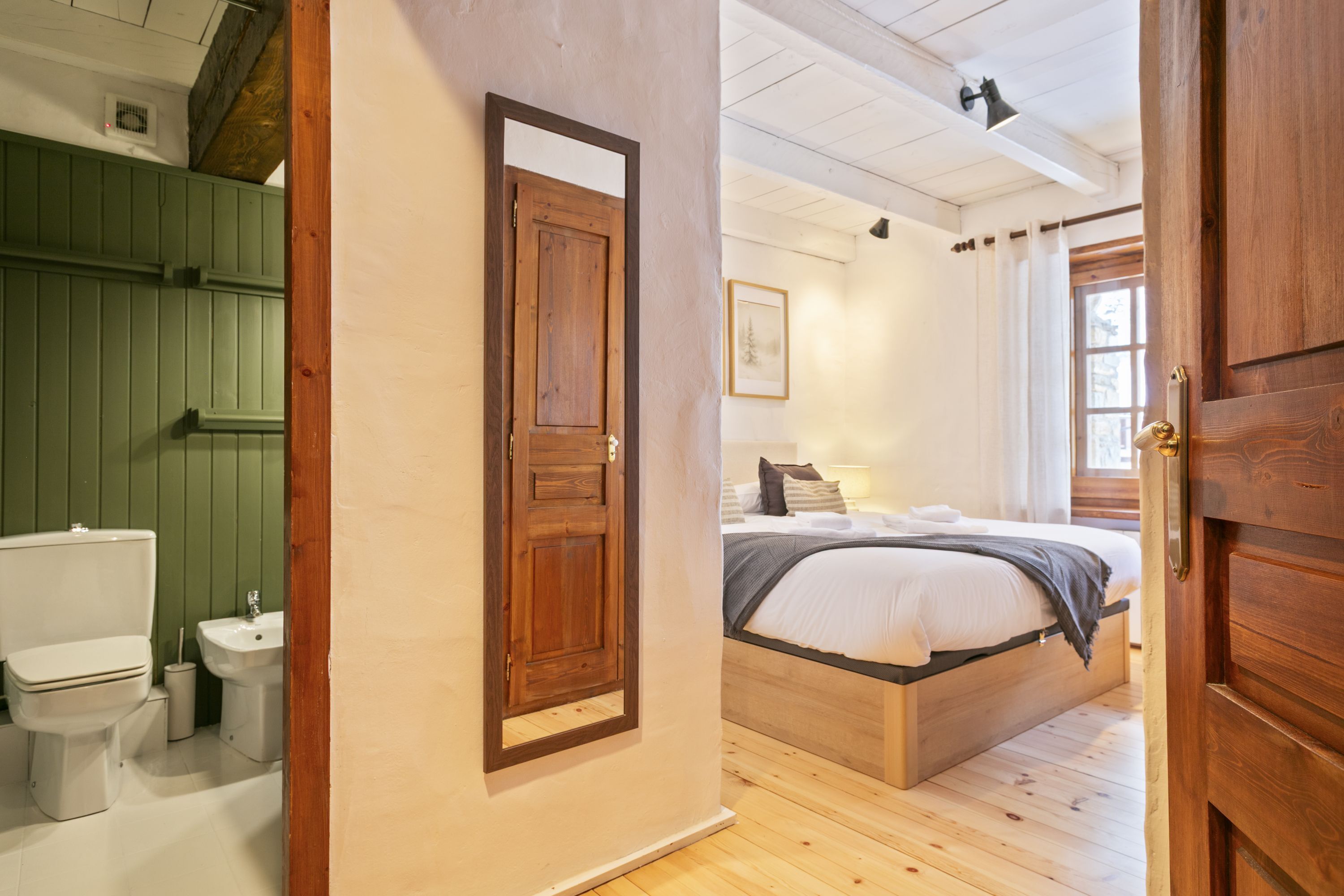 A room with a wooden door, a bed with white bedding, a bedside table, a window with curtains, and a green wall.