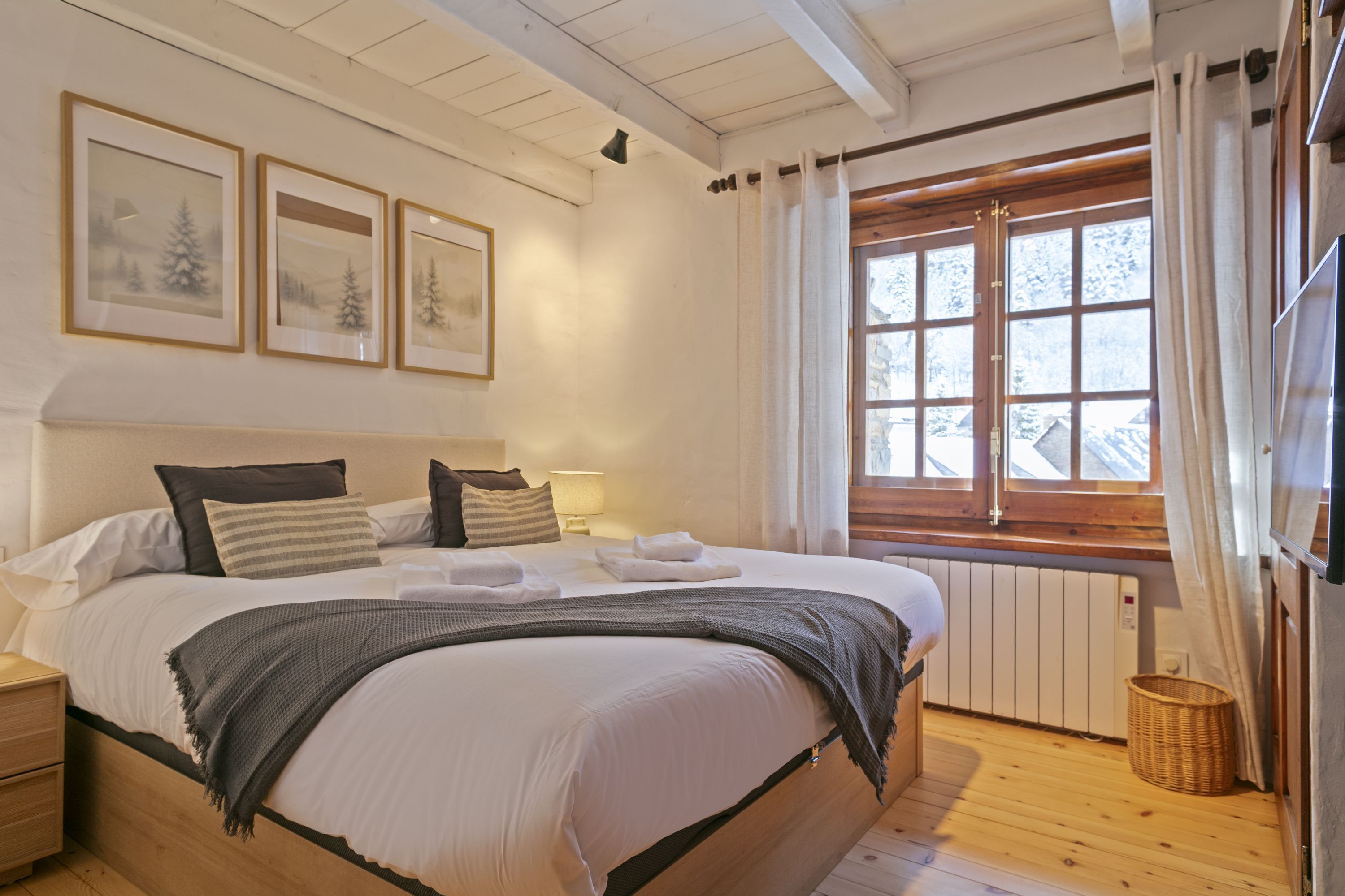 Une chambre confortable avec un grand lit, une tête de lit en bois, une fenêtre avec des rideaux et des tableaux encadrés accrochés au mur.