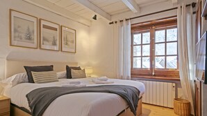 Et hyggeligt soveværelse med en stor seng, et træhovedgærde, et vindue med gardiner og billeder i rammer på væggen.