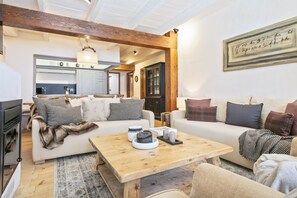 Un salon avec un canapé, une table basse et une cheminée. On aperçoit une cuisine au fond.