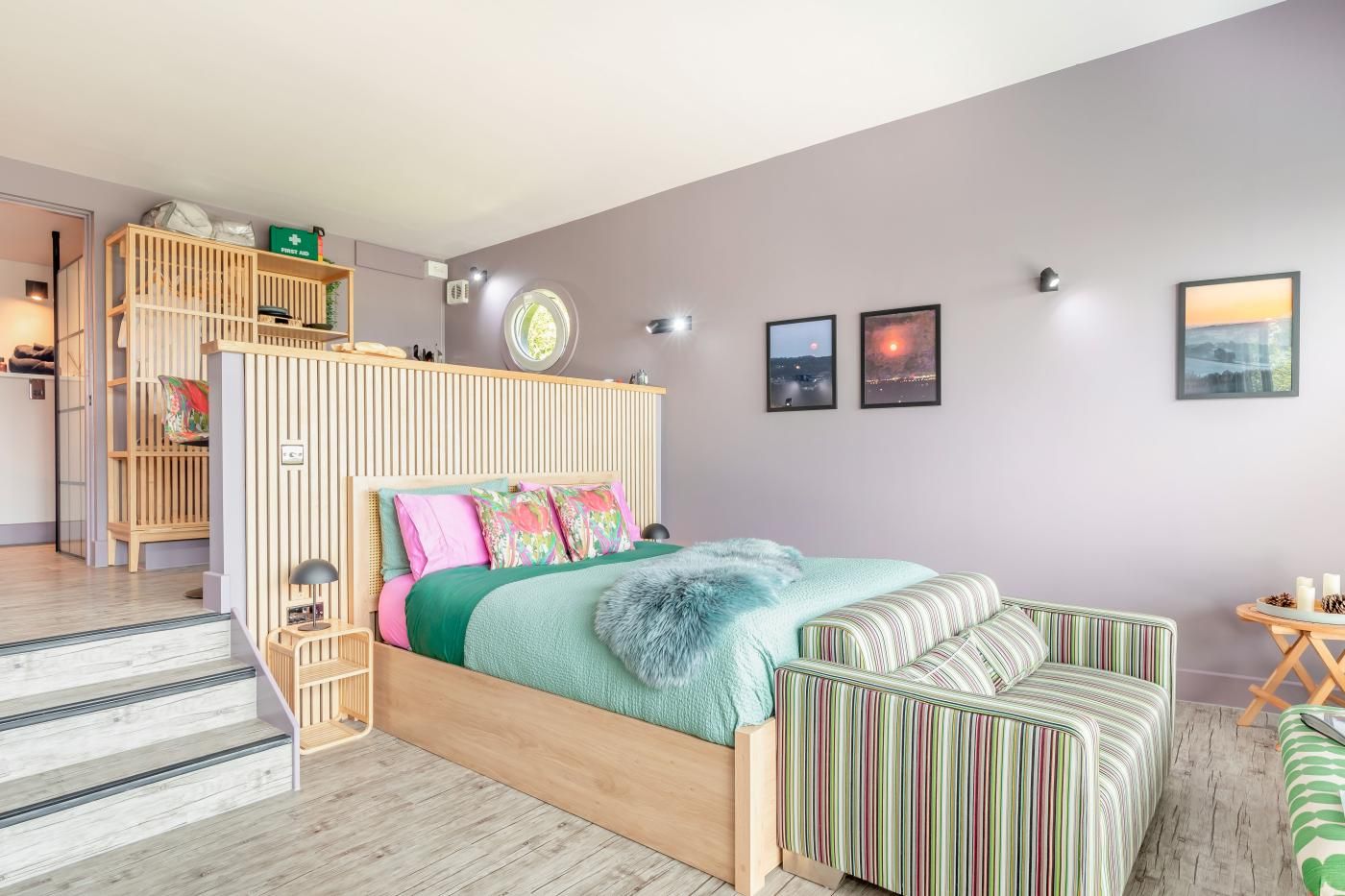 A bedroom with a bed, a wooden headboard, a striped sofa, a small table with candles, and a staircase.
