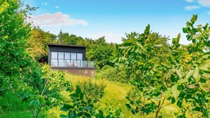 Ein modernes Haus mit einem großen Glasfenster, umgeben von üppiger Vegetation.