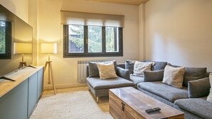 Ein modernes Wohnzimmer mit einer Sofagarnitur, einem Holztisch, einer Stehlampe und einem Fenster mit Blick auf Grünflächen.