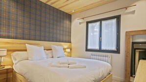 Ein Schlafzimmer mit einem hölzernen Kopfteil, einem großen Bett mit weißer Bettwäsche, einem Fenster mit Vorhängen und einem Heizkörper.