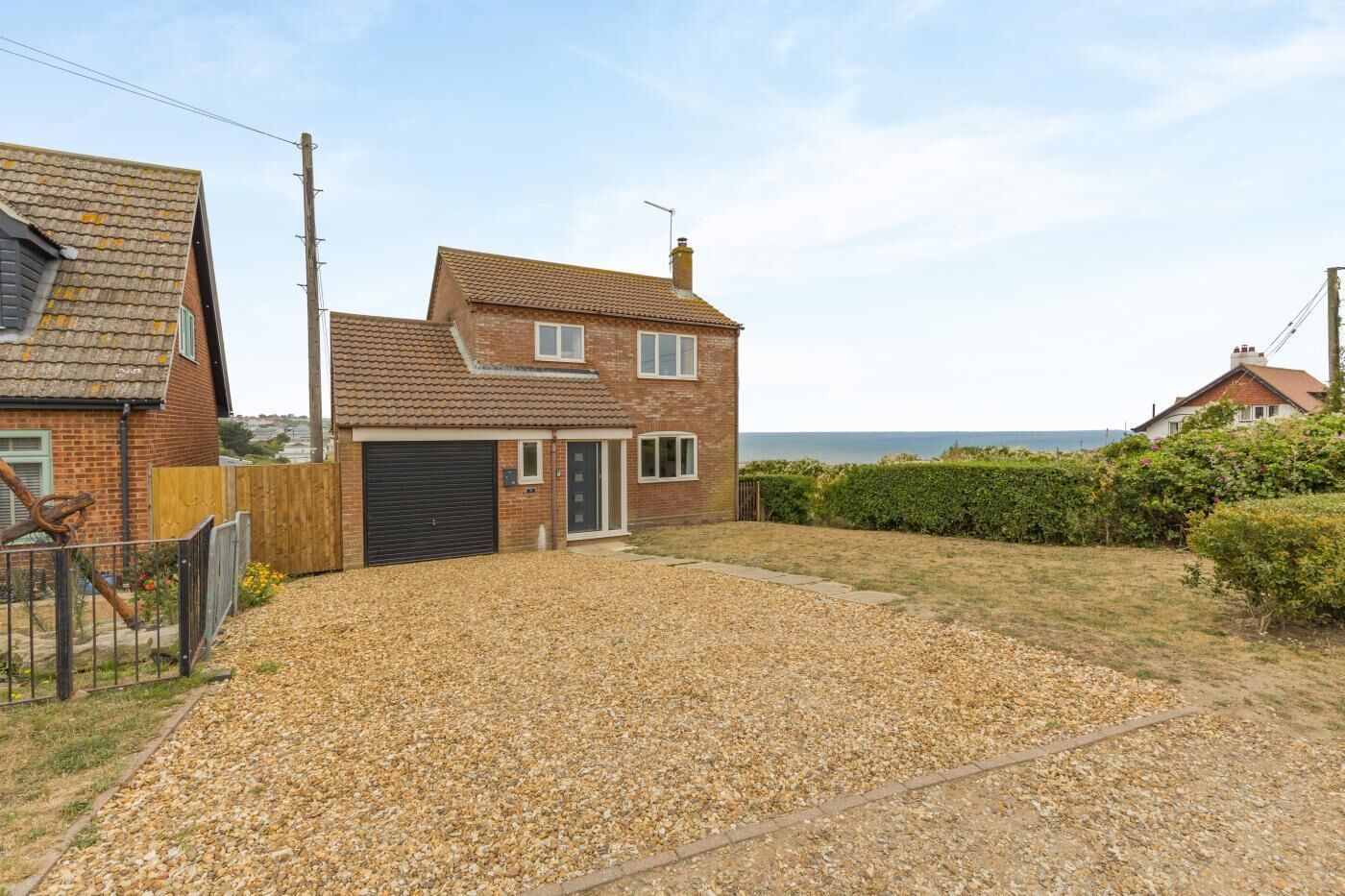 A two-story house with a gravel driveway, a garage, and a view of the sea.
