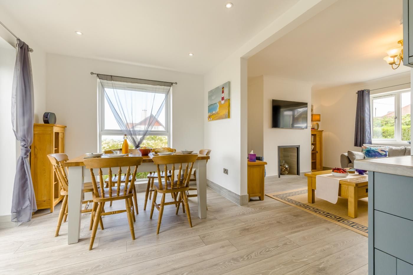 A spacious living area with a dining table, chairs, a fireplace, and a TV mounted on the wall.