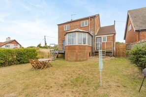A two-story house with a brick exterior, a conservatory, and a backyard with a table and chairs. - 3 Bed in Mundesley (oc-s44224) (Mundesley)