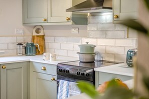 A kitchen with a stove, a pot on top, and two white mugs with floral designs. - 3 Bed in Newnham (oc-r41757) (Newnham-on-Severn)