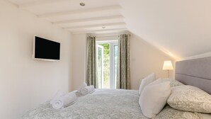 A bedroom with a bed, a TV, a window with curtains, and a lamp. - 2 Bed in Croyde (oc-g44729) (Croyde)
