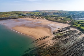 Eine Vogelperspektive zeigt eine Küstenlandschaft mit einem Sandstrand, felsigen Klippen und einer Stadt im Hintergrund.
