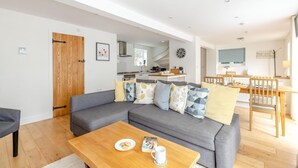 A modern living room with a grey sofa, wooden coffee table, and a dining area with wooden chairs and a table. - 2 Bed in Croyde (oc-g44729) (Croyde)