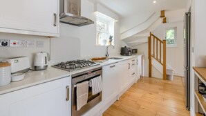 A modern kitchen with white cabinets, a gas stove, a microwave, and a large window. - 2 Bed in Croyde (oc-g44729) (Croyde)