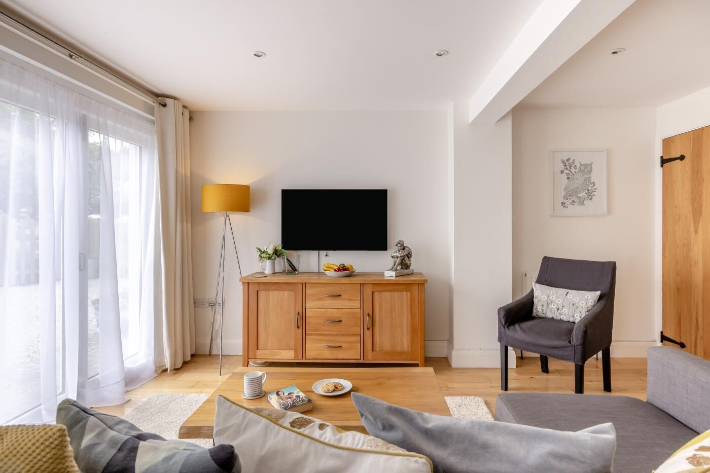 En moderne stue med et fladskærms-tv, et træskab, en grå lænestol og en sofa.