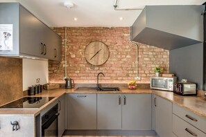 A modern kitchen with a brick wall, stainless steel appliances, and a clock. - 4 Bed in Skirlaugh (oc-w43303) (Skirlaugh)
