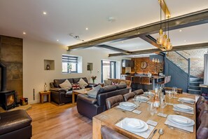 A modern living space with a fireplace, leather sofas, a dining table set for six, and a kitchen area with a brick wall. - 4 Bed in Skirlaugh (oc-w43303) (Skirlaugh)