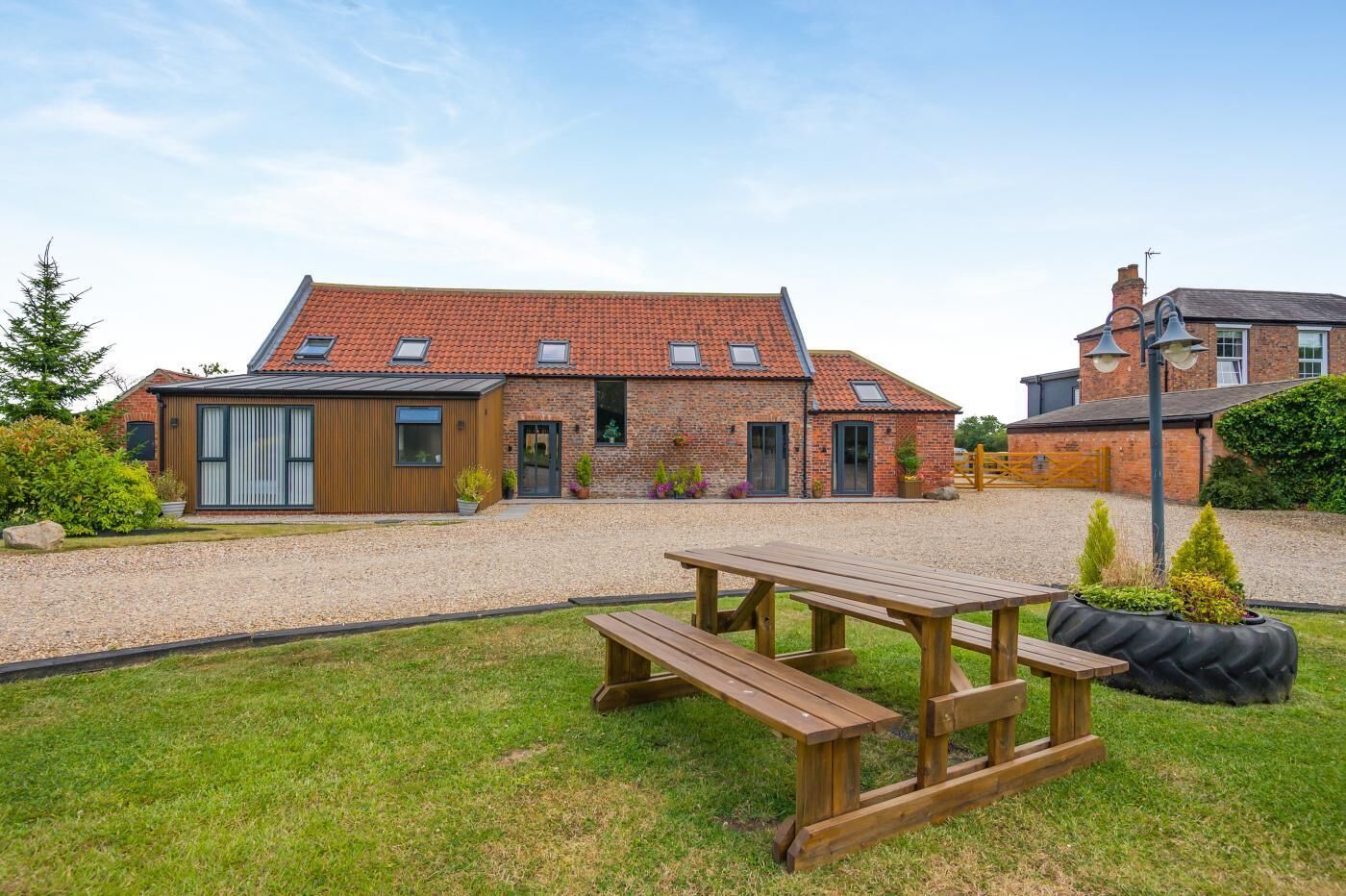 A brick house with a gravel driveway, a wooden picnic table, and a small garden area.