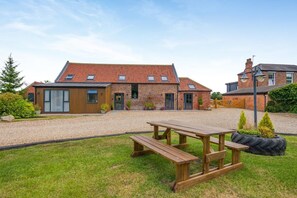 A brick house with a gravel driveway, a wooden picnic table, and a small garden area. - 4 Bed in Skirlaugh (oc-w43303) (Skirlaugh)
