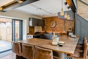 A modern kitchen with a large island, a brick wall, and a dining area with leather chairs. - 4 Bed in Skirlaugh (oc-w43303) (Skirlaugh)