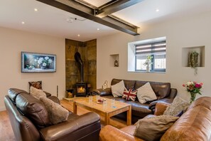 A living room with a fireplace, leather sofas, a coffee table, and a painting on the wall. - 4 Bed in Skirlaugh (oc-w43303) (Skirlaugh)