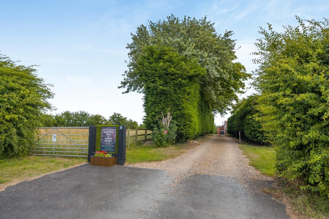 A gravel path leading to a gated entrance with a sign for Field House Farm Holiday Cottages.