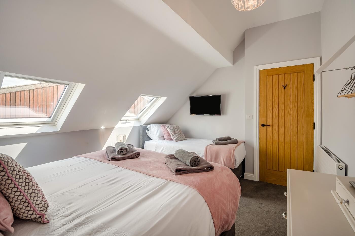 A bedroom with two beds, a skylight, a television, and a wooden door.