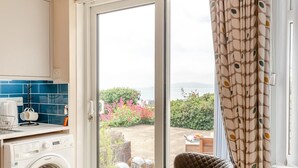 A room with a washing machine, a coffee maker, and a view of a garden and sea. - 2 Bed in Weymouth (oc-s42788) (Weymouth)