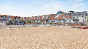 A coastal residential area with houses, a pebbled beach, and parked cars. - 2 Bed in Weymouth (oc-s42788) (Weymouth)