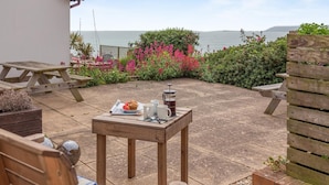 A patio with a wooden table set for breakfast, a view of the sea, and a wooden fence. - 2 Bed in Weymouth (oc-s42788) (Weymouth)
